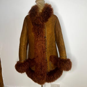 May include: A vintage brown shearling coat with a faux fur collar, cuffs, and front trim. The coat has a button-up closure and gold stitching details. The coat is displayed on a mannequin.