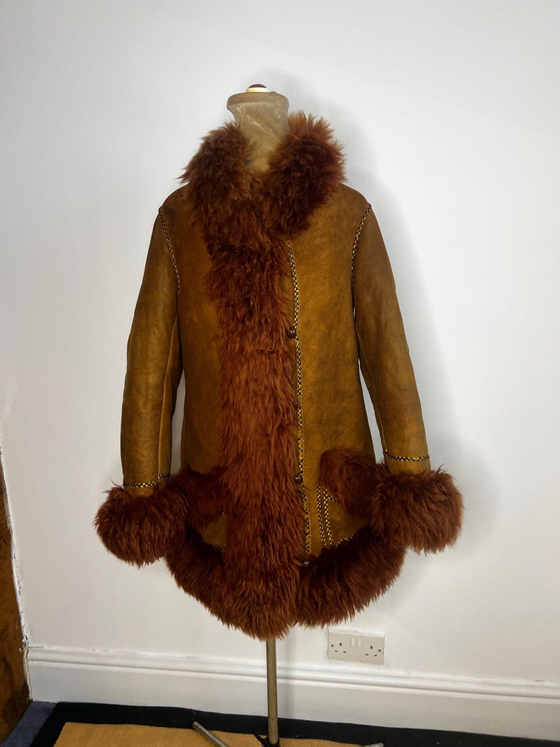 May include: A vintage brown shearling coat with a faux fur collar, cuffs, and front trim. The coat has a button-up closure and gold stitching details. The coat is displayed on a mannequin.