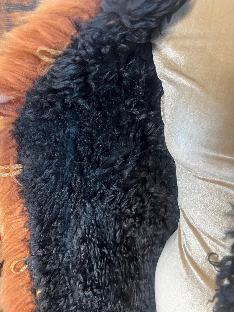 May include: Close-up of a coat featuring a combination of textures and colors. The coat has a black, curly fur lining, a tan-colored fur trim, and a beige satin-like fabric on the right side.