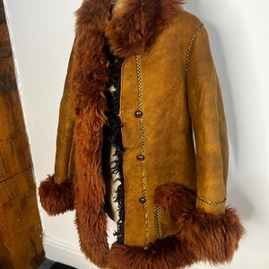 May include: A vintage brown suede coat with a faux fur collar, cuffs, and trim. The coat features a button-up front and decorative stitching. The fur trim is a rich, reddish-brown color, and the coat is displayed on a mannequin.