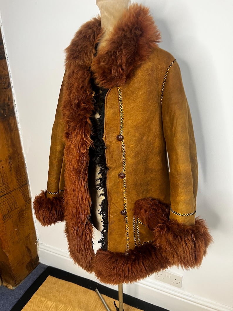 May include: A vintage brown suede coat with a faux fur collar, cuffs, and trim. The coat features a button-up front and decorative stitching. The fur trim is a rich, reddish-brown color, and the coat is displayed on a mannequin.