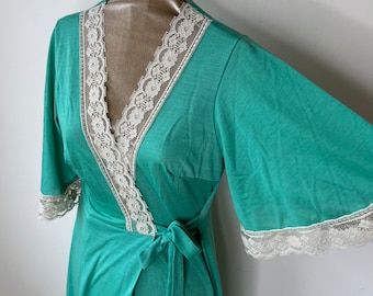 May include: A teal green wrap dress with a white lace trim around the neckline and sleeves. The dress has a tie at the waist.