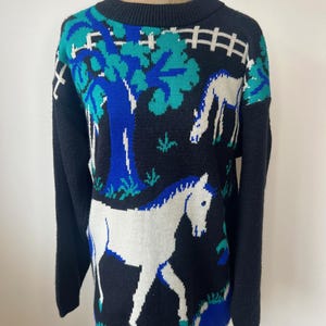 May include: Black sweater with a white horse and tree design. The sweater has blue and green accents.