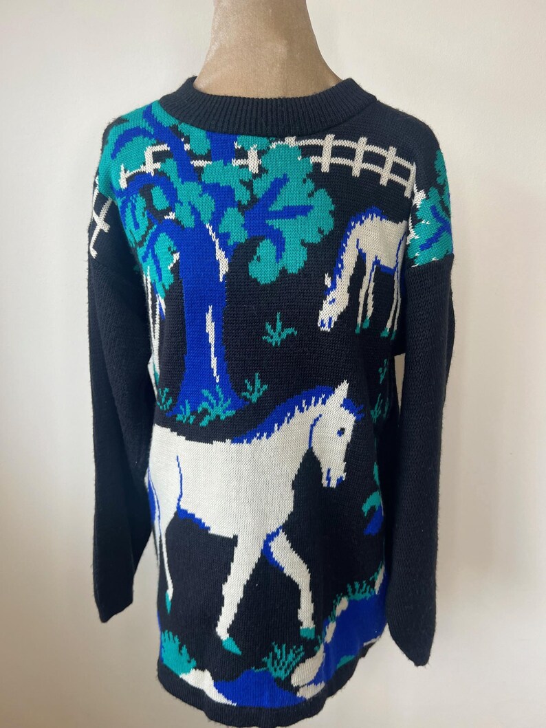 May include: Black sweater with a white horse and tree design. The sweater has blue and green accents.
