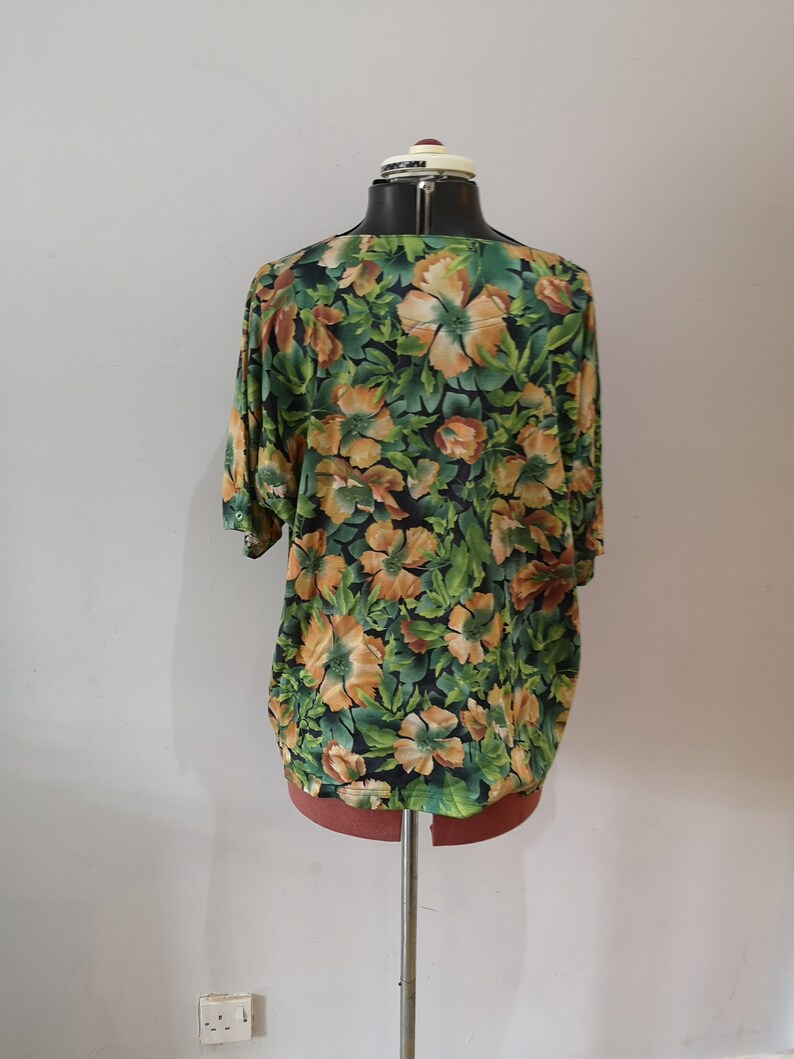 May include: A green and orange floral print blouse with a scoop neck and short sleeves.