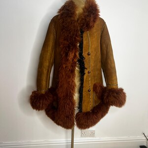 May include: A vintage brown suede coat with a faux fur collar, cuffs, and trim. The coat features a button-up front and decorative stitching. The fur is a deep reddish-brown color, and the coat is displayed on a mannequin.