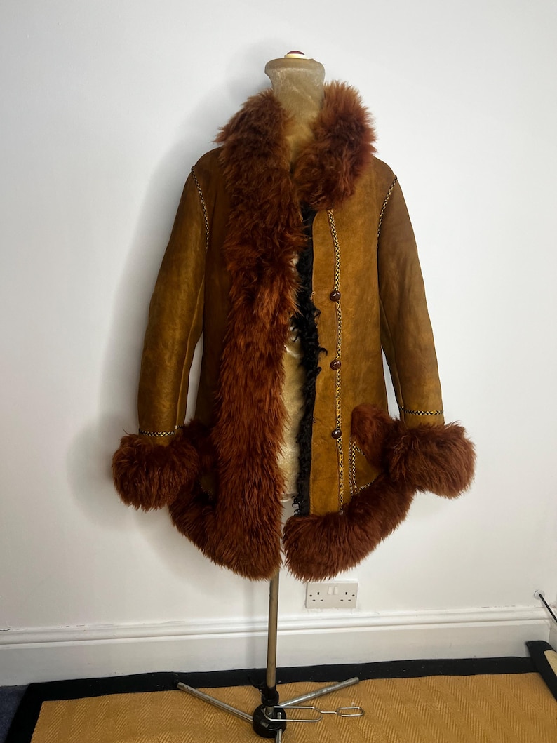 May include: A vintage brown suede coat with a faux fur collar, cuffs, and trim. The coat features a button-up front and decorative stitching. The fur is a deep reddish-brown color, and the coat is displayed on a mannequin.