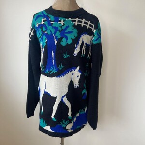 May include: Black sweater with a white horse and tree design in blue and green.