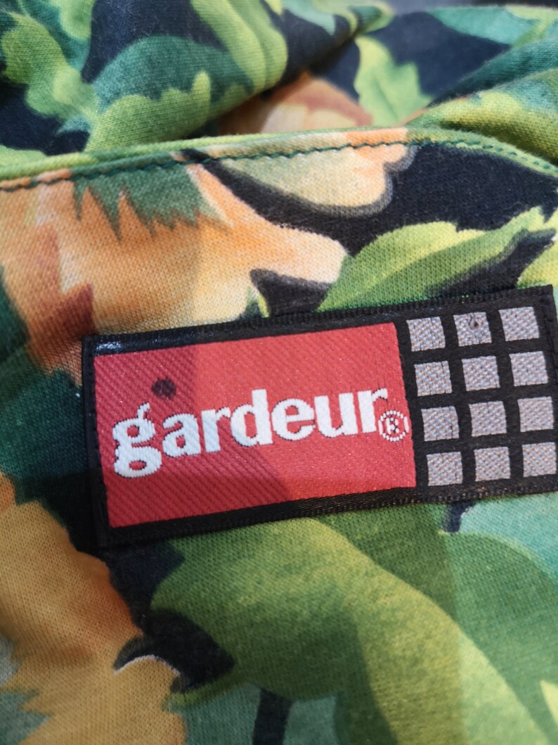May include: A red and black rectangular label with the word "gardeur" in white lettering and a registered trademark symbol. The label is attached to a green and orange fabric with a floral pattern.