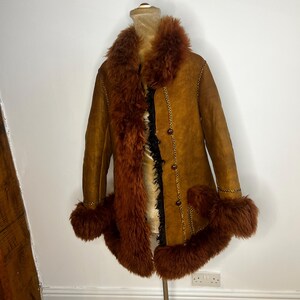 May include: A vintage brown suede coat with a faux fur collar, cuffs, and trim. The coat features a button-up front and decorative stitching. The coat is displayed on a mannequin.