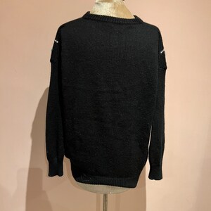 May include: Black knitted sweater with a white and blue patterned design on the shoulders.