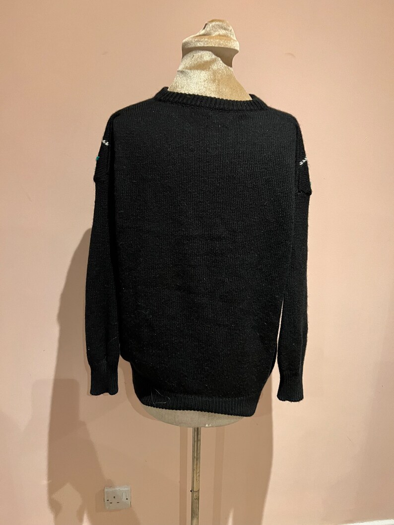 May include: Black knitted sweater with a white and blue patterned design on the shoulders.