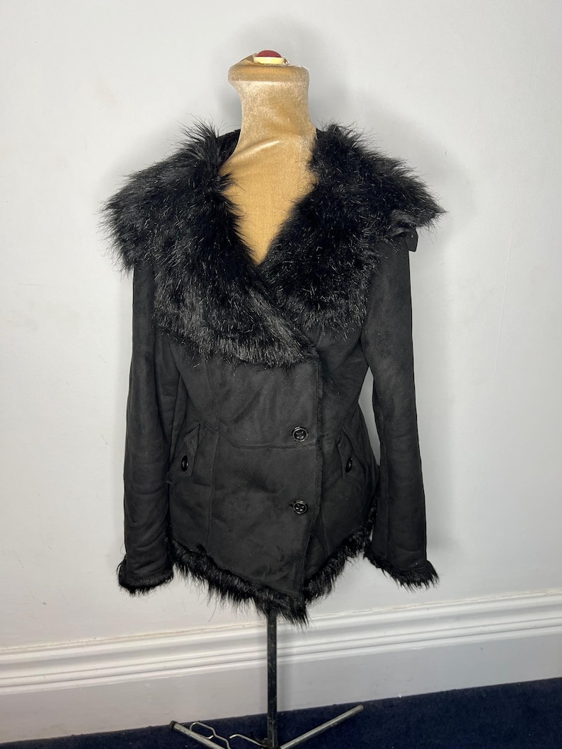 May include: A black faux fur collar jacket with a double breasted closure and a faux fur trim around the hem.