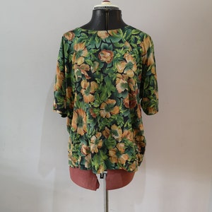 May include: A green and orange floral print blouse with short sleeves on a mannequin.