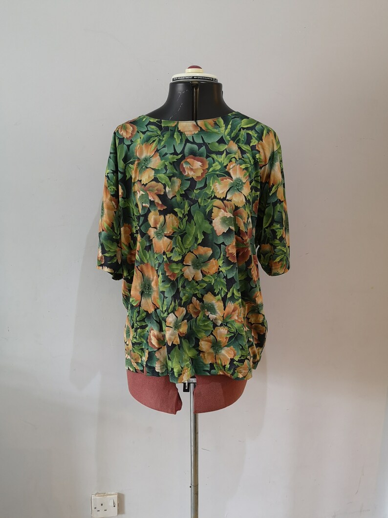 May include: A green and orange floral print blouse with short sleeves on a mannequin.