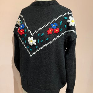 May include: Black sweater with a white and teal chevron pattern and embroidered flowers in red, blue, and white.