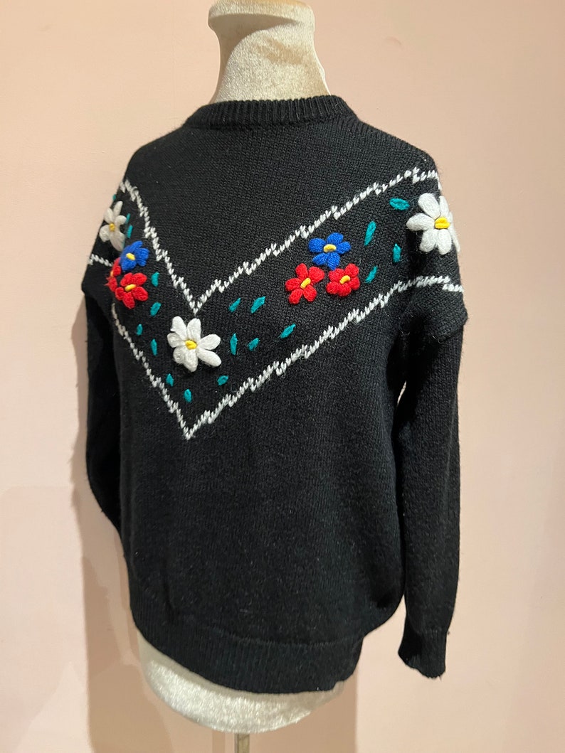 May include: Black sweater with a white and teal chevron pattern and embroidered flowers in red, blue, and white.