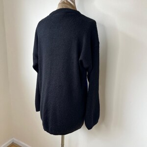 May include: Black knitted sweater with a crew neck and long sleeves. The sweater is on a mannequin.