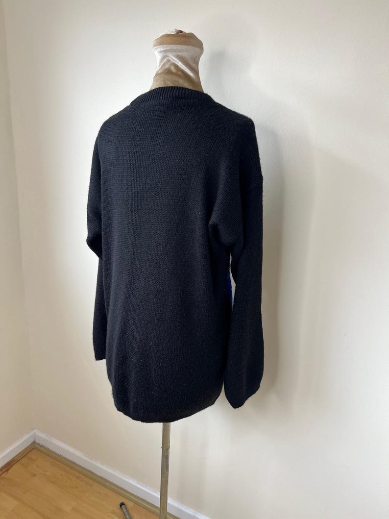 May include: Black knitted sweater with a crew neck and long sleeves. The sweater is on a mannequin.