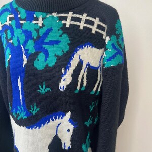 May include: Black knitted sweater with a white horse and blue and green trees design.