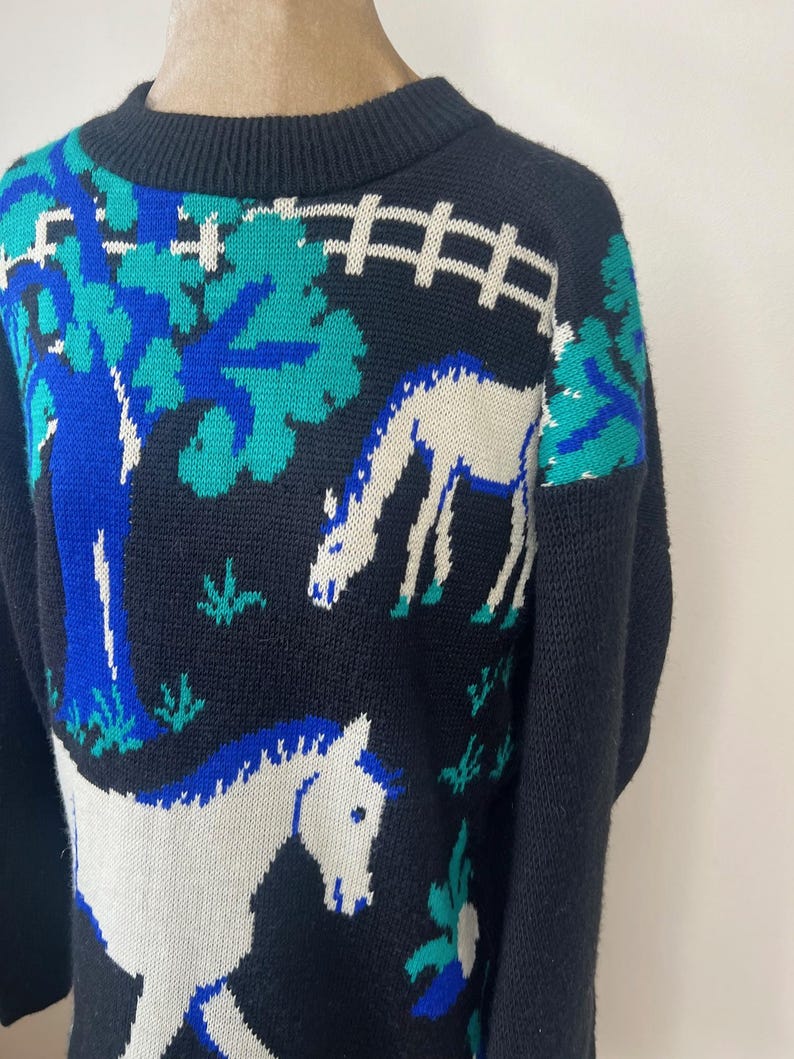 May include: Black knitted sweater with a white horse and blue and green trees design.