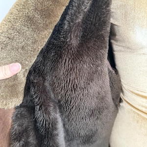 May include: Close-up of a brown coat interior with a dark brown, plush lining. The coat's exterior is a lighter shade of brown, with a soft, textured appearance. The image highlights the warmth and texture of the garment.