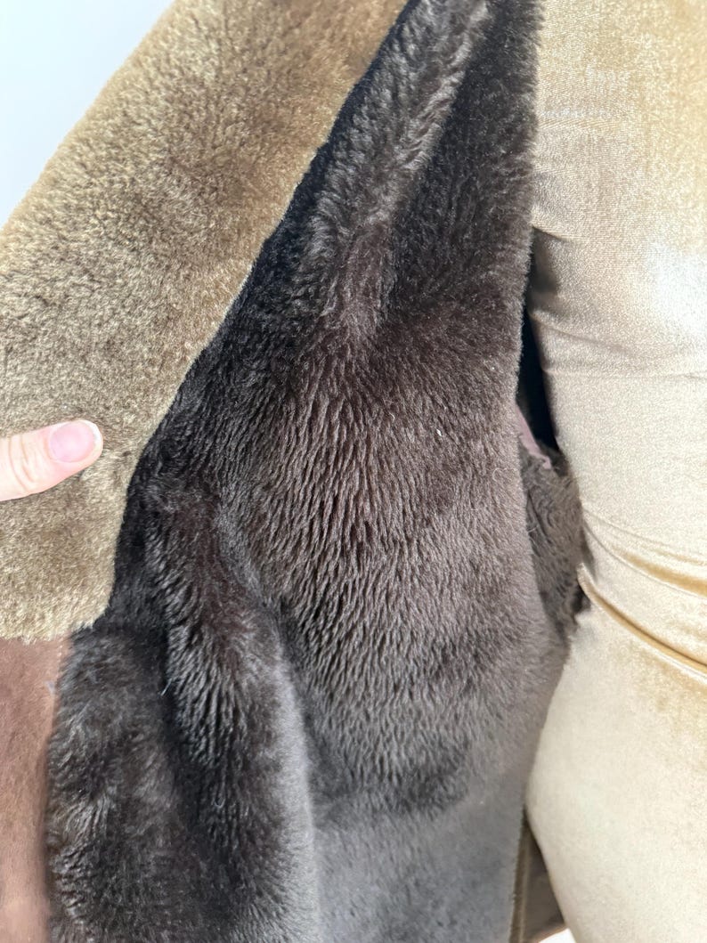 May include: Close-up of a brown coat interior with a dark brown, plush lining. The coat's exterior is a lighter shade of brown, with a soft, textured appearance. The image highlights the warmth and texture of the garment.