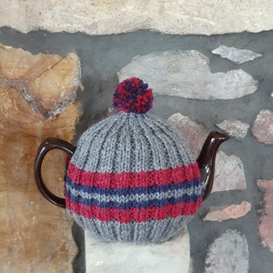 May include: Grey knitted teapot cosy with red and blue stripes and a pom-pom on top.
