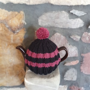 May include: Black and burgundy knitted teapot cosy with a pom pom on top.