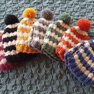 May include: Seven striped knitted hats with pom-poms in various colours, including pink, black, yellow, grey, green, orange, and blue.