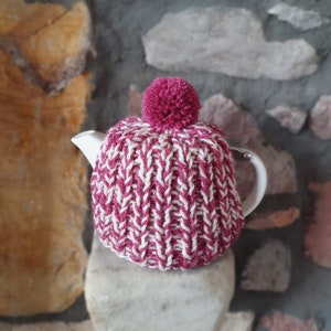 May include: A pink and white knitted teapot cosy with a pom-pom on top.