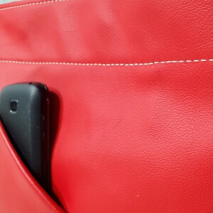 May include: A red leather bag with a white stitch detail and a black phone in the pocket.