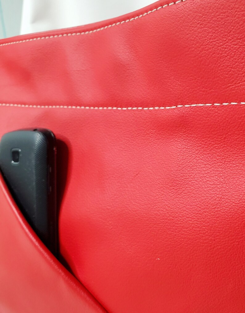 May include: A red leather bag with a white stitch detail and a black phone in the pocket.