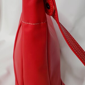 May include: A red leather shoulder bag with a white stitch detail and a silver buckle. The bag has a flap closure and a long strap.