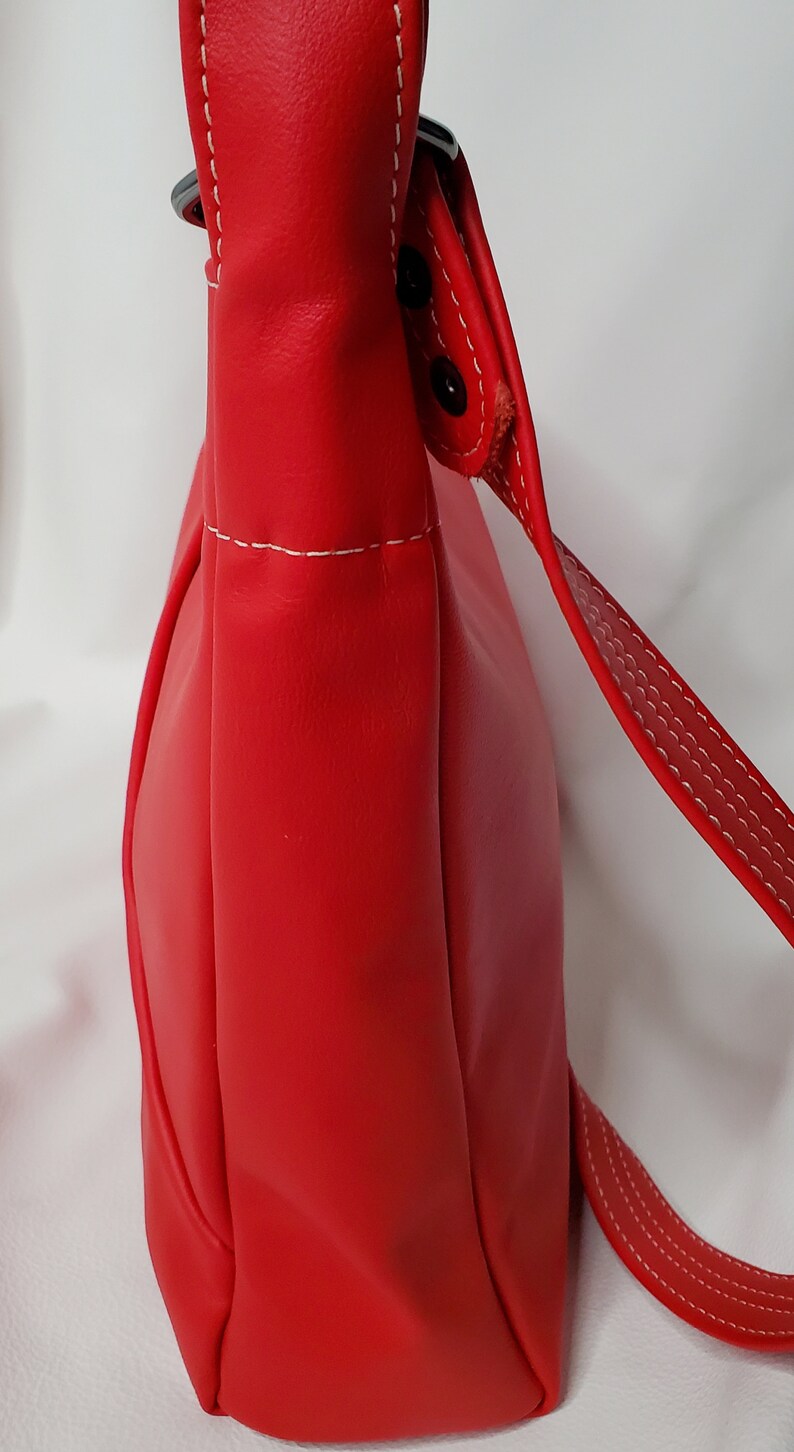 May include: A red leather shoulder bag with a white stitch detail and a silver buckle. The bag has a flap closure and a long strap.