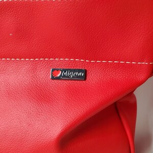 May include: Red leather handbag with a white stitched seam and a silver logo that says "Migrino" with a red heart.