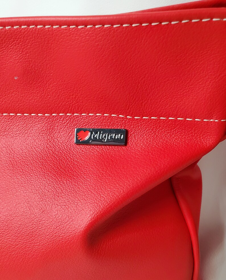 May include: Red leather handbag with a white stitched seam and a silver logo that says "Migrino" with a red heart.