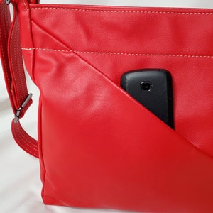 May include: A red leather crossbody bag with a white stitch detail and a black phone in the front pocket.