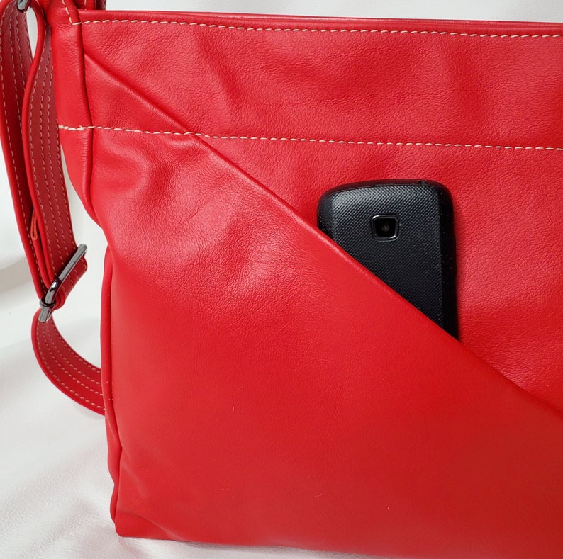 May include: A red leather crossbody bag with a white stitch detail and a black phone in the front pocket.
