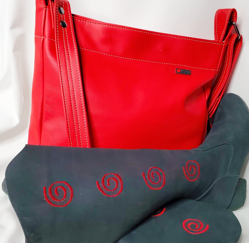 May include: A red leather handbag with a long strap and a black boot with red embroidered swirls. The handbag has a white stitching detail and a small logo.