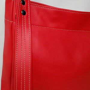 May include: Red leather handbag with a white stitched strap and two silver metal rivets.