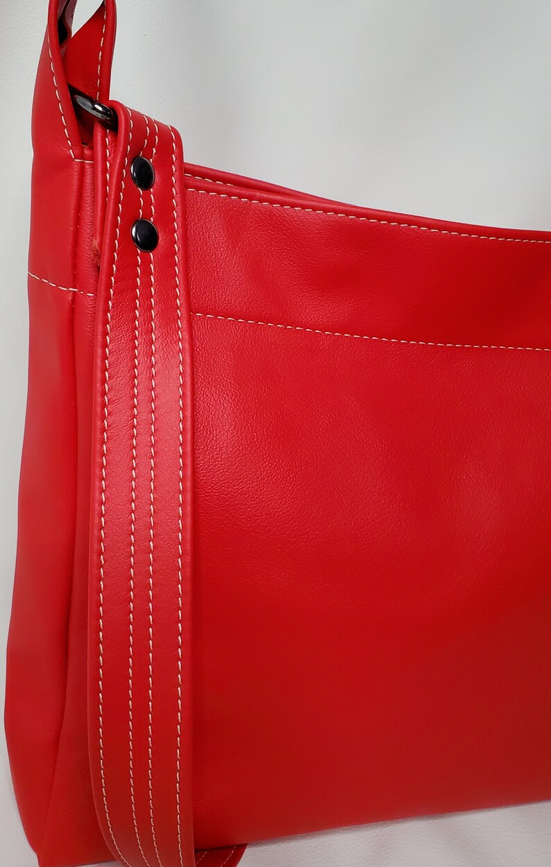 May include: Red leather handbag with a white stitched strap and two silver metal rivets.