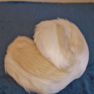 Könnte beinhalten: Ein weißer, flauschiger Schwanz für ein Kostüm oder ein Bastelprojekt. Der Schwanz besteht aus weichem, synthetischem Fell und ist etwa 60 cm lang.