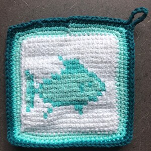 May include: A teal and white crocheted pot holder with a fish design. The pot holder has a loop for hanging.