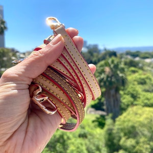 May include: A close-up of a beige leather strap with yellow and red stitching. The strap is folded in half and held in a hand.