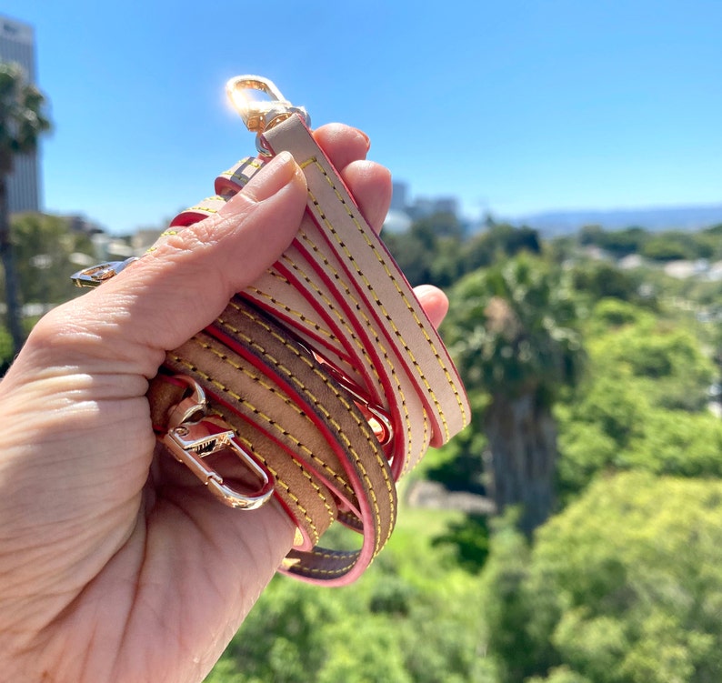 May include: A close-up of a beige leather strap with yellow and red stitching. The strap is folded in half and held in a hand.