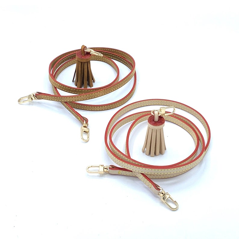 May include: Two leather straps with red stitching and tassels. The straps are brown and beige and have gold clasps.