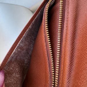 May include: Open brown leather wallet with a gold zipper. The interior shows a lighter brown lining with a textured surface. The wallet is partially open, revealing the inside.