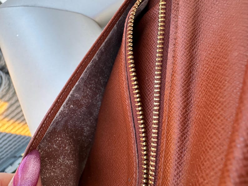 May include: Open brown leather wallet with a gold zipper. The interior shows a lighter brown lining with a textured surface. The wallet is partially open, revealing the inside.
