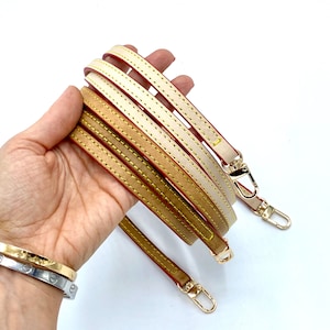 May include: Three leather straps with gold hardware and red stitching. The straps are beige, brown, and cream.